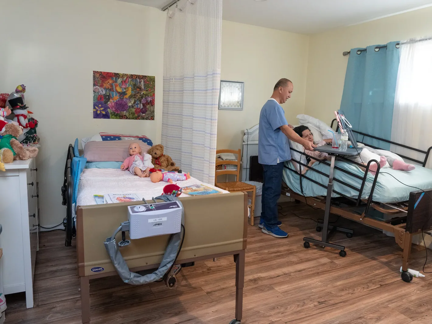 Caregiver providing personalized assistance to resident in comfortable shared bedroom equipped with hospital bed and home-like amenities