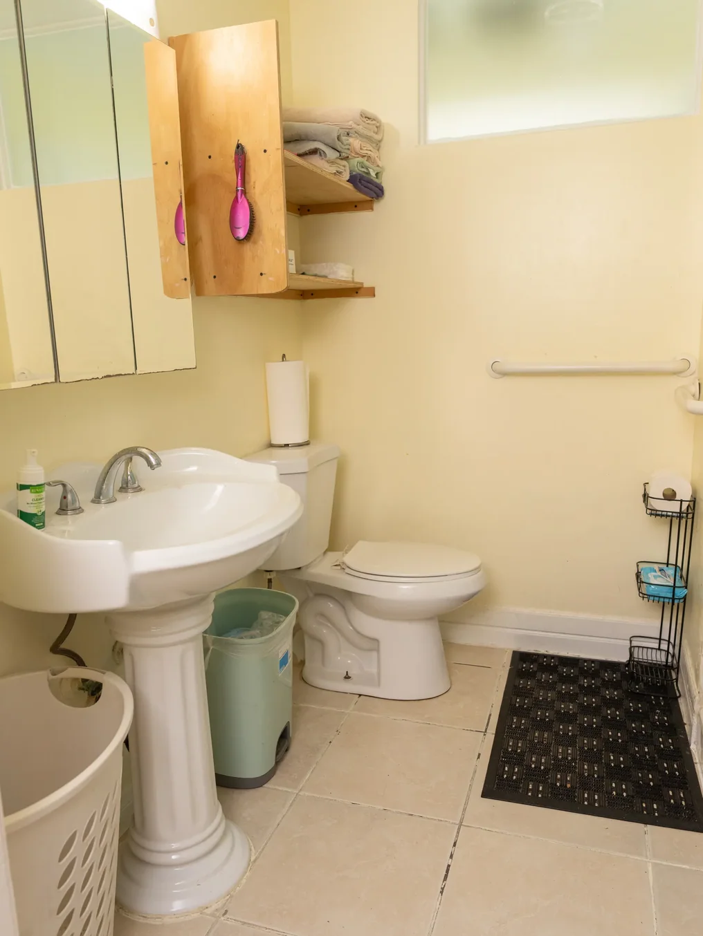 Clean accessible bathroom featuring pedestal sink, toilet, safety grab bars, and organized storage shelves
