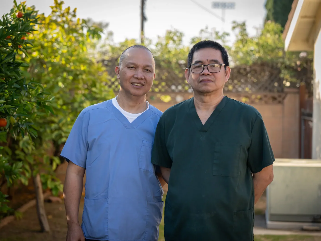 Two friendly caregivers in medical scrubs smiling together in an outdoor setting with plants