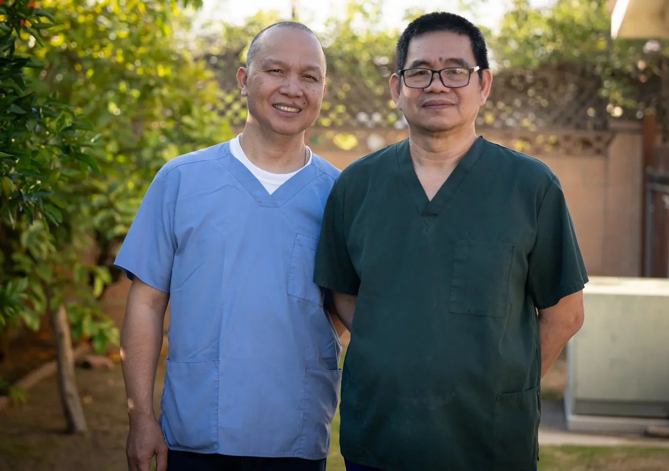 Two caregivers in medical scrubs smiling outdoors at residential care facility